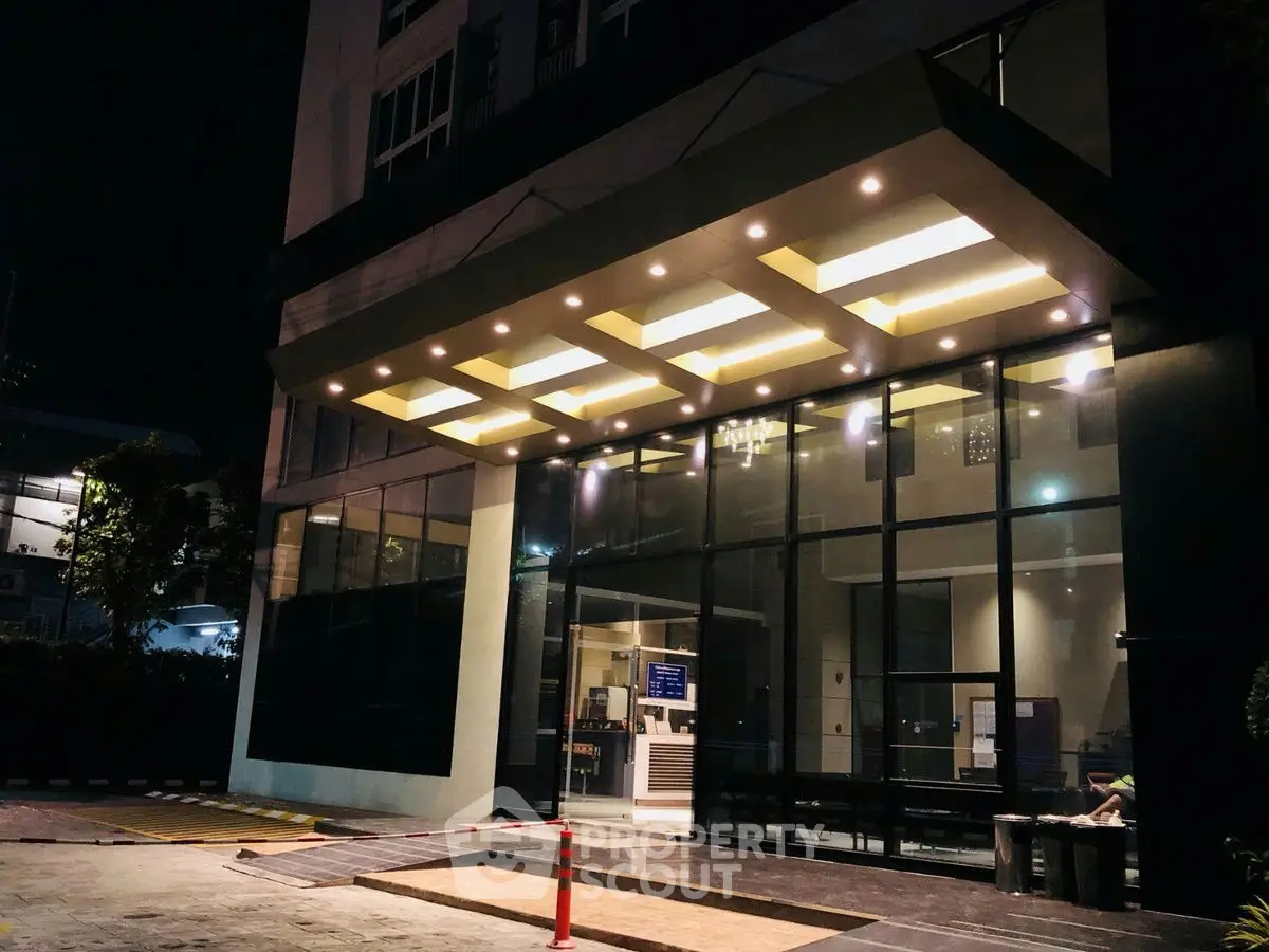 Modern building entrance with illuminated canopy and glass facade at night.