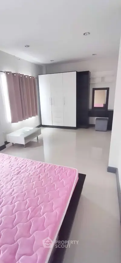Spacious bedroom with modern wardrobe and pink mattress in a bright, airy apartment.