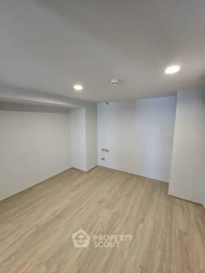 Spacious empty room with wooden flooring and recessed lighting, ideal for customization.