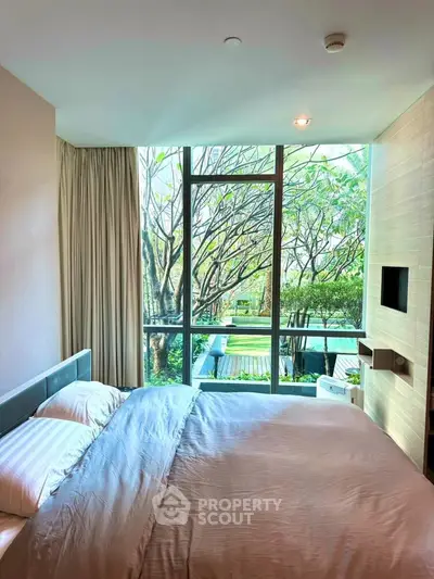 Luxurious bedroom with large window offering serene garden view, modern decor, and cozy ambiance.