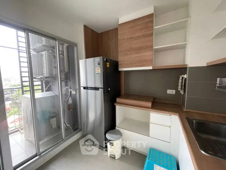 Modern kitchen with sleek cabinets and balcony view, featuring stainless steel fridge and washing machine.