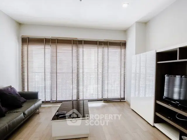 Modern living room with sleek furniture and large windows with blinds.