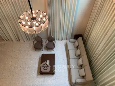 Elegant living room with high ceiling and chandelier, featuring a cozy sofa and armchairs.