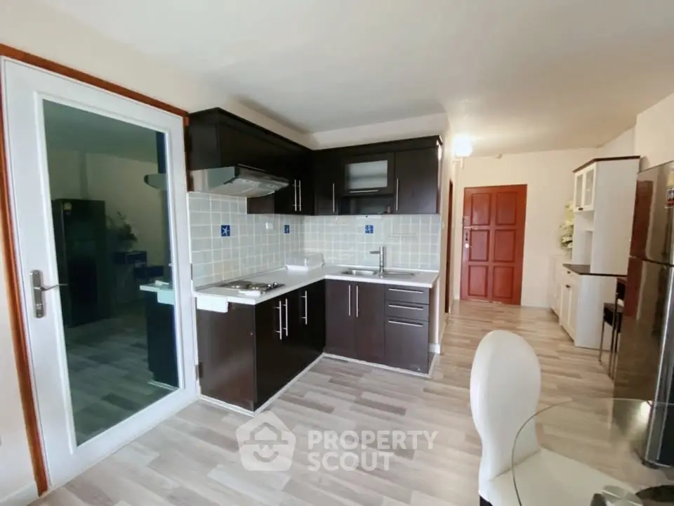Modern kitchen with dark cabinets and sleek flooring, featuring open layout and glass door access.