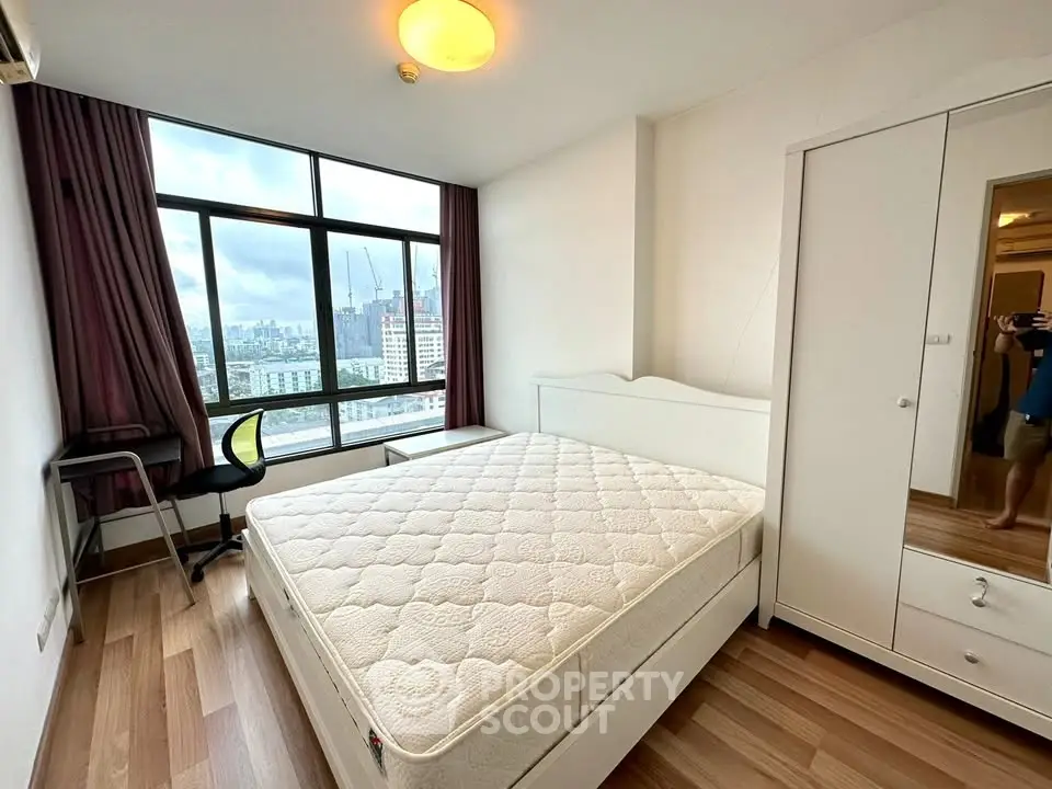Bright bedroom with large window offering city views, featuring a comfortable bed and modern furnishings.