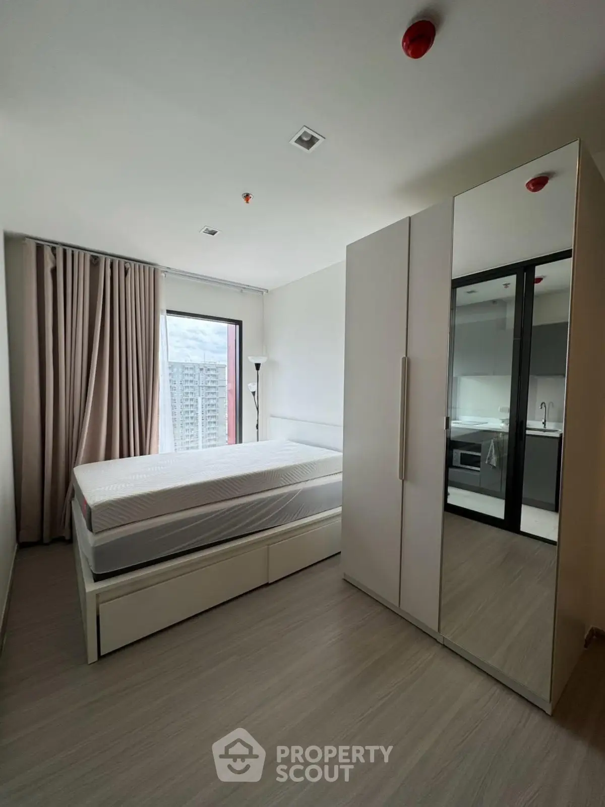 Modern bedroom with large window and mirrored wardrobe in high-rise apartment.