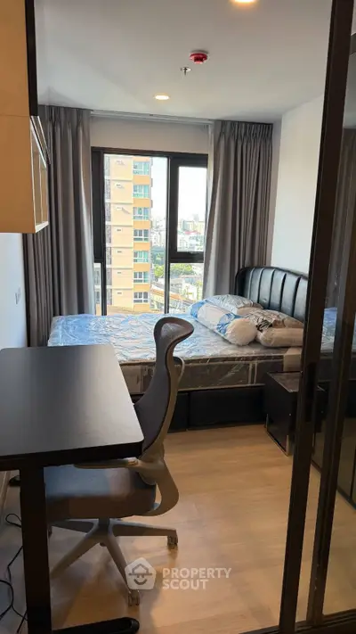 Modern bedroom with city view, featuring a sleek desk and comfortable chair.