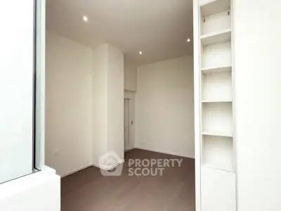 Spacious modern room with built-in shelves and large window, perfect for versatile living space.