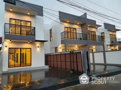 Modern twin townhouses with sleek white facades and striking black accents, featuring spacious balconies and secure gated parking, captured at dusk with warm lighting.