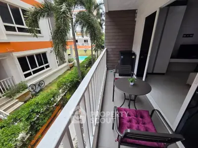 Charming balcony with cozy seating overlooking lush garden and pool in modern apartment complex.
