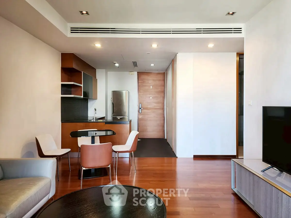 Modern open-plan living room with sleek kitchen and dining area, featuring wooden flooring and contemporary furniture.