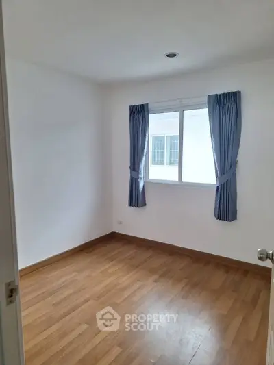Bright empty room with wooden flooring and window with blue curtains, ideal for customization.