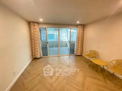 Spacious living room with herringbone flooring and glass doors leading to a sunlit balcony.
