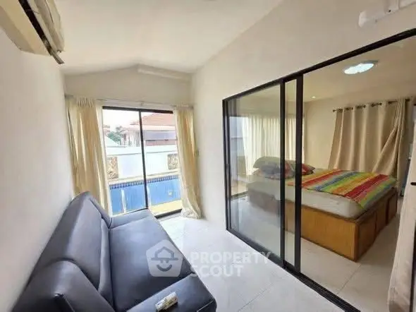 Cozy bedroom with glass partition and balcony view, featuring modern sofa and colorful bedding.