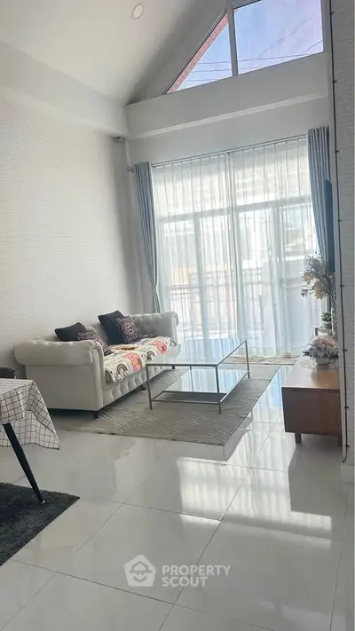 Spacious living room with high ceilings and large windows offering natural light and modern decor.