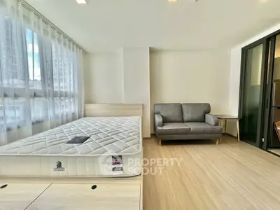 Modern bedroom with large windows, cozy sofa, and sleek wooden flooring in a bright apartment.