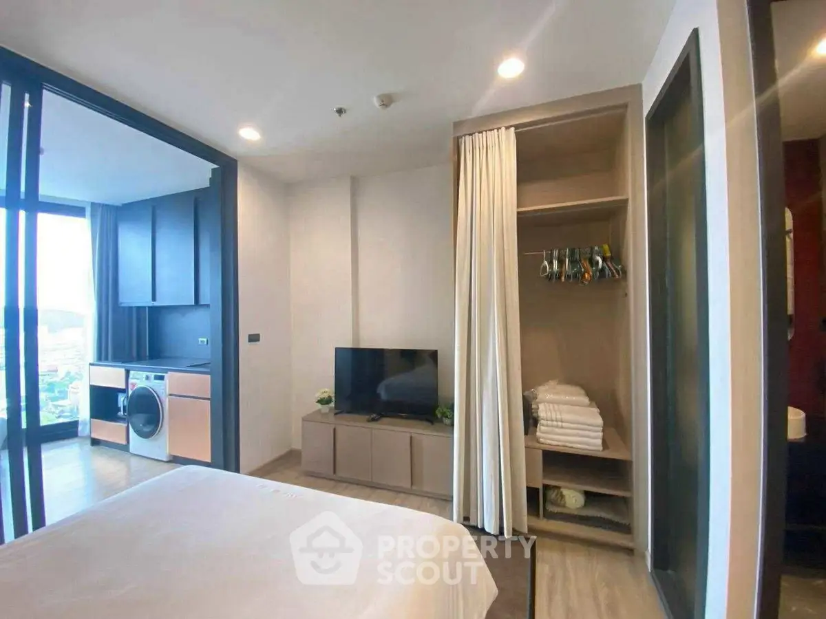 Modern bedroom with open closet and in-unit laundry, featuring a sleek design and city view.