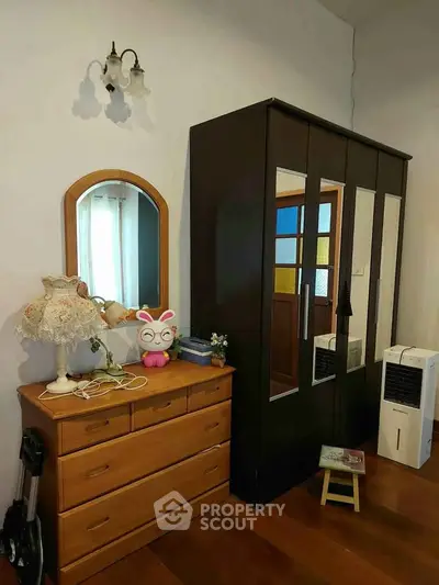 Cozy bedroom with wooden furniture and decorative lamp, featuring a wardrobe and dresser.