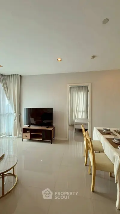 Modern living room with dining area and TV, featuring elegant decor and natural light.