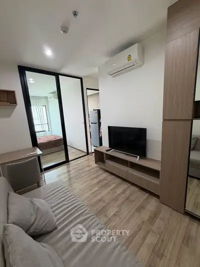 Modern living room with wooden flooring, cozy sofa, and sleek TV setup in a stylish apartment.