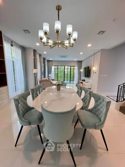 Elegant dining area with plush chairs and modern chandelier in a spacious living room setting.