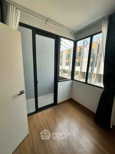 Modern room with large windows and balcony access, featuring sleek wooden flooring and contemporary design.