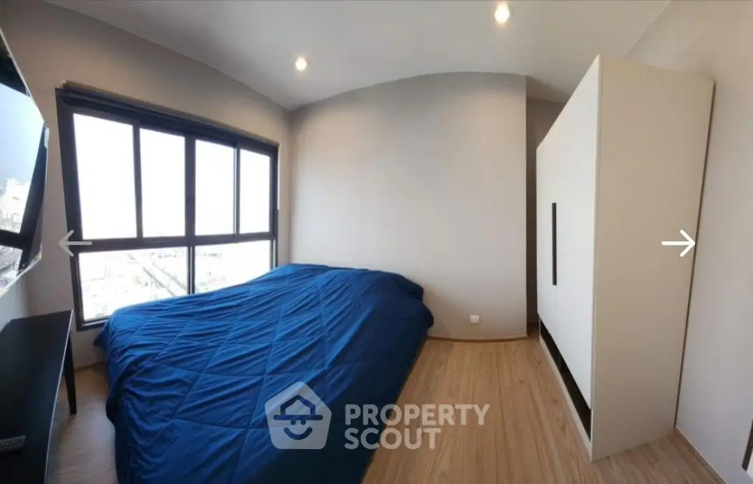 Modern bedroom with large window and blue bedding in a stylish apartment.