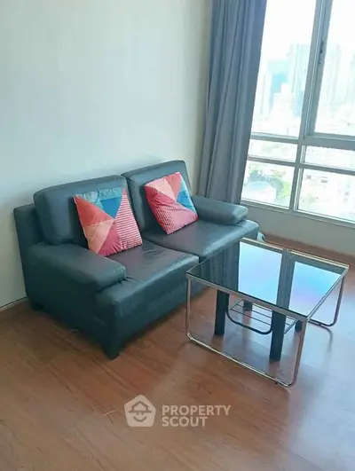 Modern living room with sleek sofa and glass coffee table, offering a bright city view through large windows.