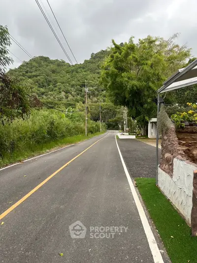 Scenic road with lush greenery and mountain view, ideal for serene living.