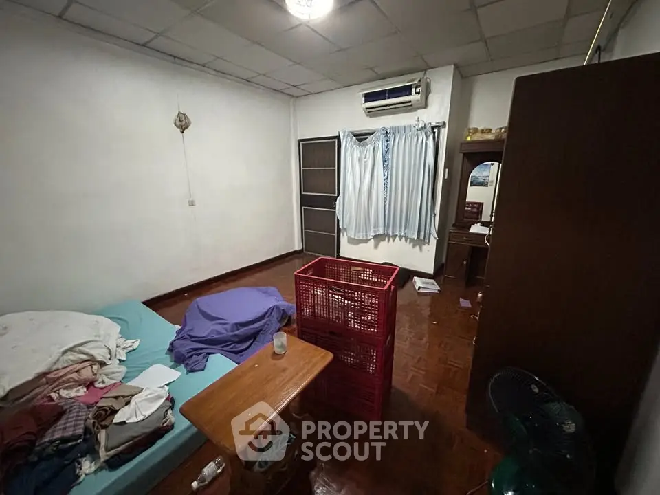 Cozy bedroom with air conditioning and wooden flooring, featuring a simple layout and natural light.