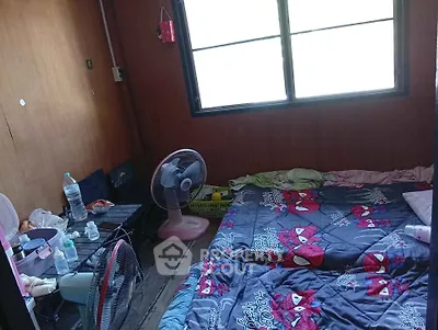 Cozy bedroom with twin beds and fan, featuring wooden walls and a bright window.
