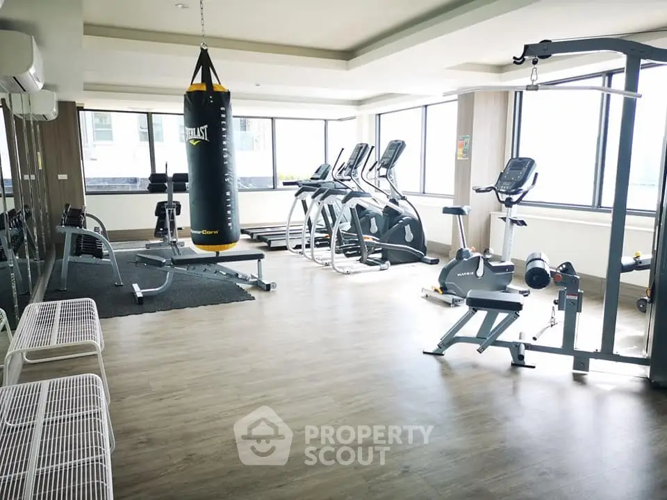 Spacious gym with modern fitness equipment and large windows for natural light.