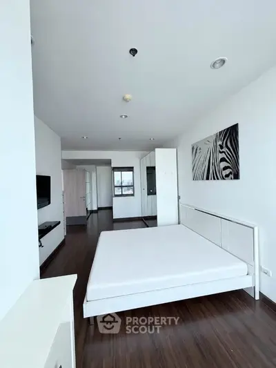 Spacious modern bedroom with minimalist decor and hardwood floors in a high-rise apartment.