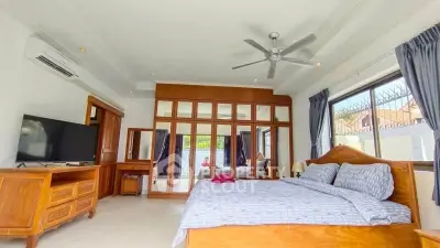 Spacious bedroom with large windows and wooden furniture, featuring a cozy bed and modern amenities.