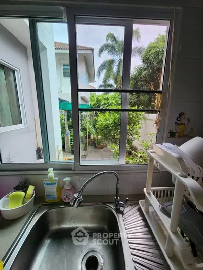 Charming kitchen view with lush greenery and modern sink setup, perfect for a serene cooking experience.