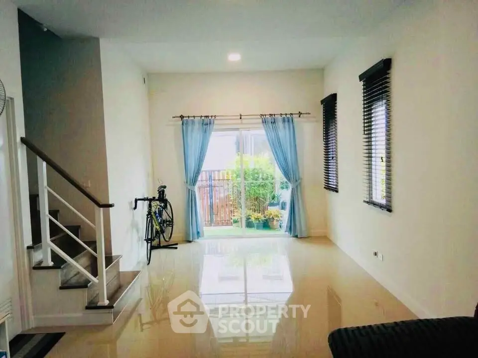 Spacious living room with glossy floors and garden view, featuring a staircase and large windows.