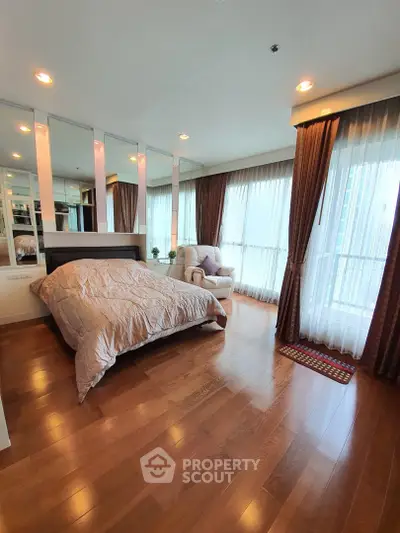Spacious bedroom with wooden flooring and large windows offering natural light.