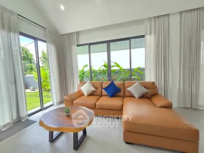 Spacious living room with modern leather sofa and large windows overlooking lush garden.