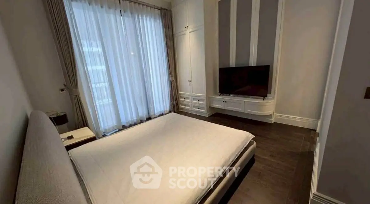 Elegant bedroom with modern decor and large window, featuring a sleek TV setup and stylish furnishings.