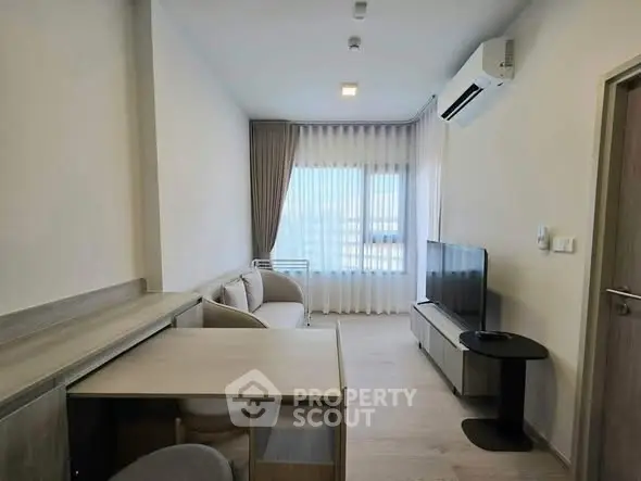 Modern living room with sleek furniture and large window, featuring a minimalist design and air conditioning.