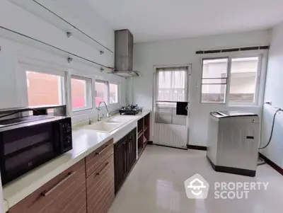 Modern kitchen with sleek countertops and appliances, featuring a microwave and washing machine.