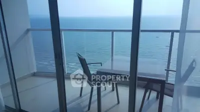 Stunning ocean view from a high-rise balcony with glass railing and outdoor seating.