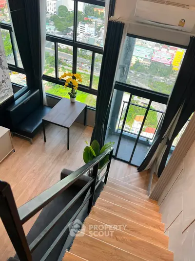 Stunning loft apartment with floor-to-ceiling windows and city view, featuring a cozy living area and balcony.