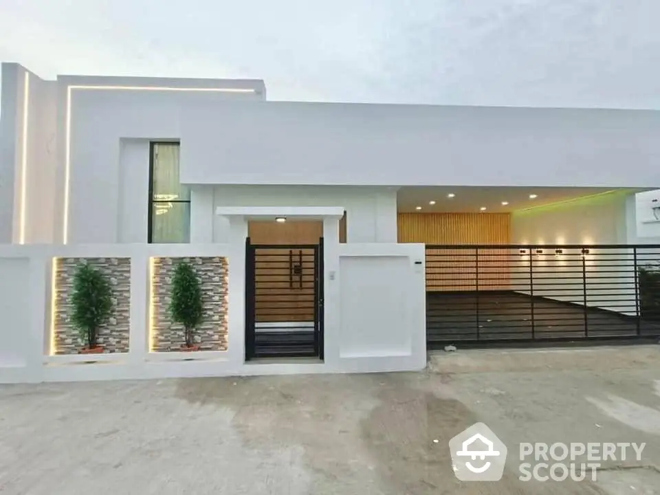 Modern single-story home with sleek white facade, warm exterior lighting, and stylish wooden garage door, offering a welcoming ambiance.