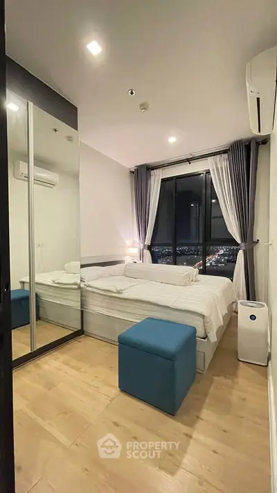 Modern bedroom with city view, mirrored closet, and cozy furnishings in a high-rise apartment.