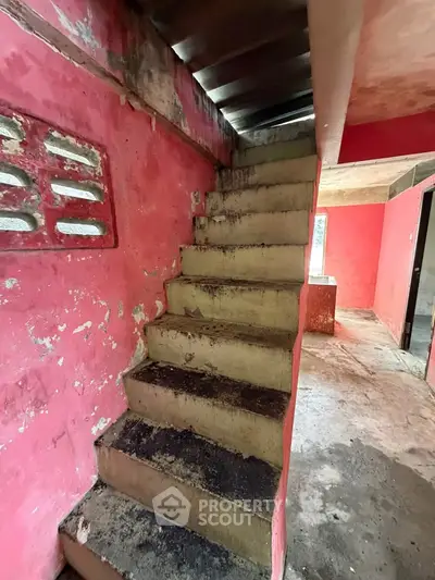 Rustic staircase in need of renovation with vibrant red walls and natural light.