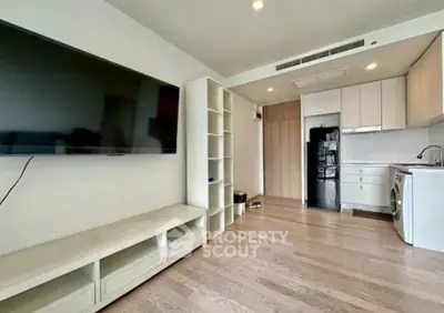 Modern living room with sleek TV, built-in shelves, and compact kitchen area featuring washing machine.