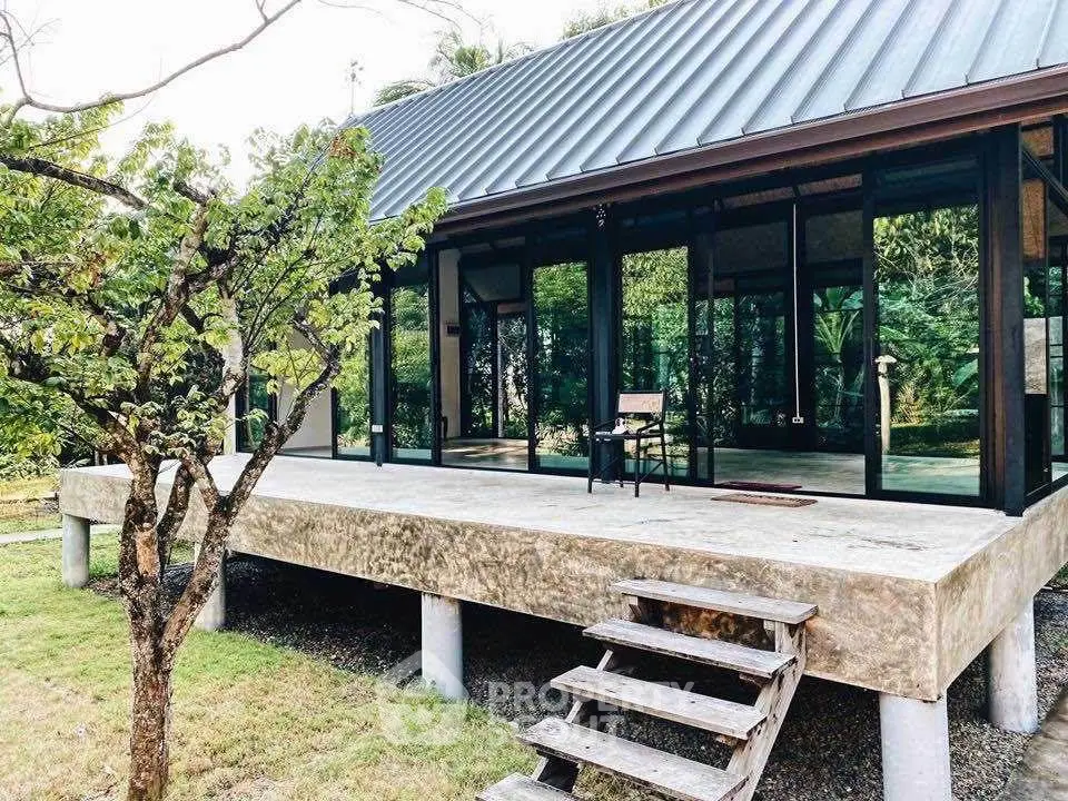 Modern glass house with elevated concrete platform and lush garden view.