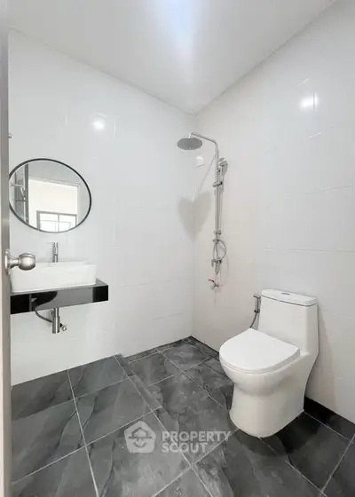 Modern bathroom with sleek fixtures and minimalist design, featuring a round mirror and elegant shower setup.