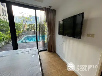 Modern bedroom with direct pool access through sliding glass doors, featuring a wall-mounted TV and wooden flooring for a cozy ambiance.